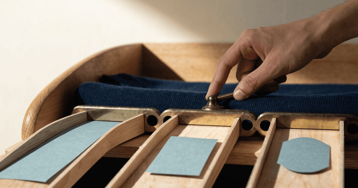 A hand adjusts a brass lever on a wooden mail-sorting desk, directing a folded navy garment into three separate channels ending in blank rectangular, square, and rounded paper tags.